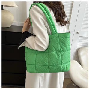 Side view of a bright green quilted puffer tote bag worn over the shoulder by a model