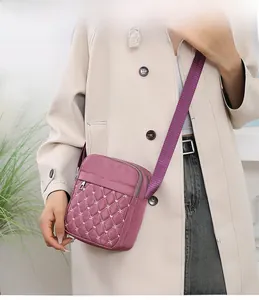 Detailed shot of purple quilted nylon crossbody bag with wide strap on a beige trench coat