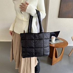 Large black quilted down tote bag with puffer design held by a model in a cozy office setting