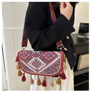 Detailed close-up of ethnic embroidered crossbody bag with colorful tassels and wide strap