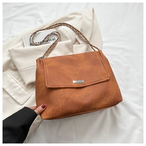 Close-up of vintage brown leather bag with silver chain strap on beige blazer