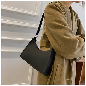 Close-up of a matte black hobo bag with gold zipper detail on a wool coat outfit