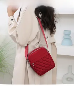Close-up of a red quilted nylon crossbody bag featuring silver zippers and adjustable strap