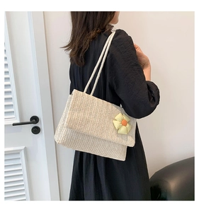 Detail of a beige woven straw tote bag with a yellow plaid flower and braided rope straps
