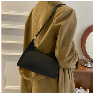 Close-up of minimalist black matte leather underarm bag with gold metal hardware