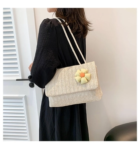 Detail view of woven straw tote bag with plaid flower decoration worn on shoulder