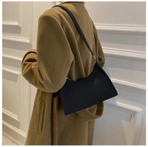 Detail of minimalist black leather baguette bag on model with camel coat in lifestyle setting