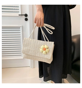 Detail of beige straw woven flap shoulder bag with a colorful floral accent on white rope strap