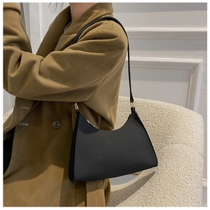 Detail of a black hobo bag with gold hardware worn over a camel wool coat on a sofa