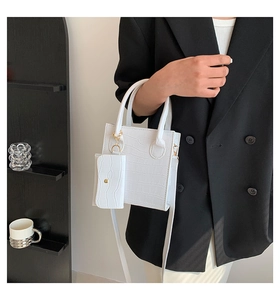 Detailansicht einer weißen Handtasche mit Krokodilprägung und kleinem Seitenbeutel