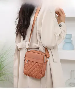 Brown quilted oxford cloth crossbody bag with multi-layer zippers on a beige trench coat
