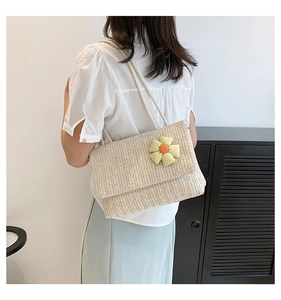 Detailed close-up of woven straw tote bag with green floral ornament and thin strap