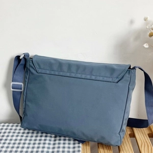 Classic navy blue nylon messenger bag with large flap and adjustable strap on a wooden rack