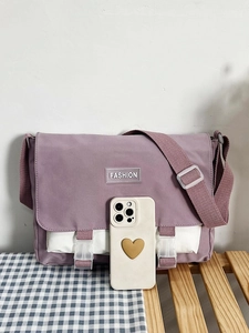 Detailed close-up of a purple and white canvas messenger bag with fashion label and buckles