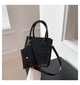 Detail der schwarzen Handtasche mit Krokodilprägung, Hochglanzfinish und kleinem Anhänger
