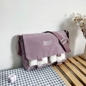 Detail of purple canvas messenger bag featuring contrast white pockets and fashion label