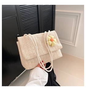 Detail of beige woven straw shoulder bag with floral accent and white cotton rope handle