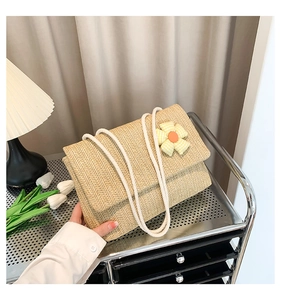 Detail of beige woven straw tote bag with a small fabric flower and white rope handle