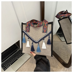 Détail du sac seau en lin bohème avec pompons colorés et poignées tissées ethniques