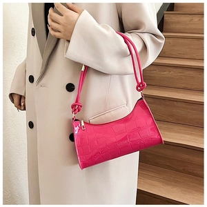 Detail of rose red crocodile pattern armpit bag with shoulder strap worn by a model