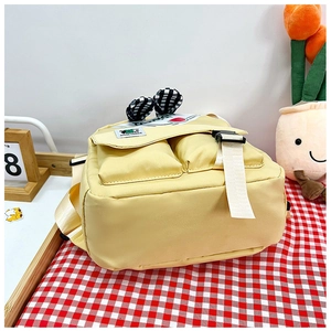 Detail view of a yellow school bag with cartoon ears and decorative buckled front pockets
