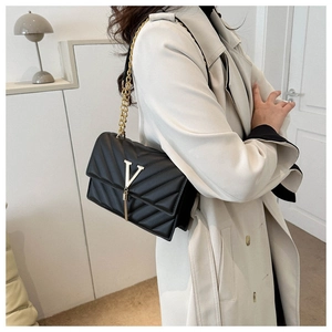Détail d'un sac bandoulière noir matelassé avec logo V doré et franges sur manteau