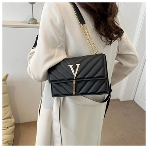 Détail d'un sac bandoulière matelassé noir avec fermoir doré en V et pompon métallique