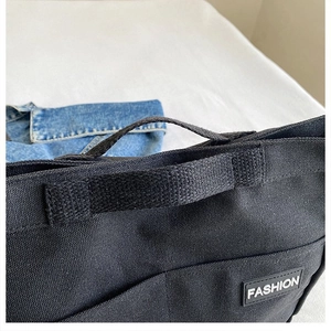 Macro detail of black canvas tote bag with fashion rubber label and heavy strap