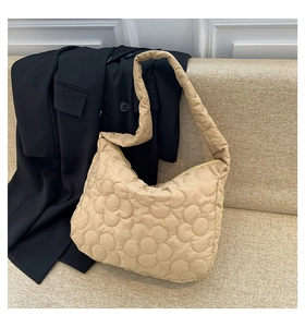 Close-up of beige quilted tote bag with floral stitching on a sofa with a black blazer
