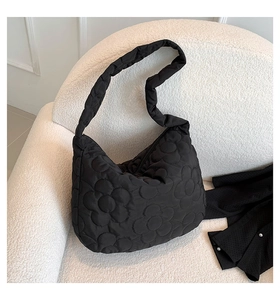 Detail view of black quilted tote bag with large flower pattern on a white sofa