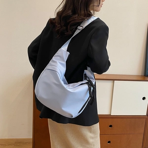 Vue latérale d'un sac bandoulière croissant bleu clair avec large sangle et tirette tressée