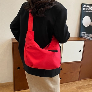Vue détaillée du dos d'un grand sac bandoulière rouge en nylon montrant sa taille sur un modèle