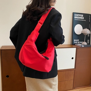 Détail du sac bandoulière rouge en nylon avec large sangle sur un mannequin en décor