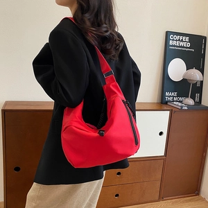 Gros plan d'un sac bandoulière croissant en nylon rouge porté par un mannequin en intérieur