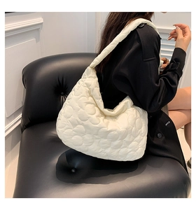 Detail of creamy white quilted tote bag featuring a floral stitched pattern and metal zipper