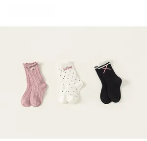 Detailed view of three pairs of girls' socks in pink, white, and black with bow accents