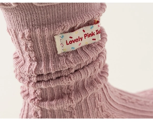 Detailed macro view of pink cable knit fabric texture with 'Lovely Pink Ic' woven label