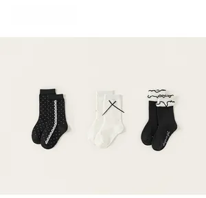 Detailed view of three pairs of girls' black and white mid-calf socks with lace and bows