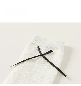 Close-up of white hollow knitted girls socks with black bow detail and textured cotton fabric
