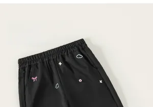 Détail du pantalon cargo noir pour fille avec broderies colorées de nuages et de nœuds