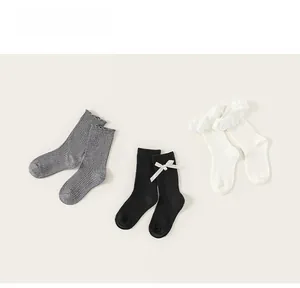 Detailed view of three pairs of ribbed socks in grey, black with bow, and lace-edged white