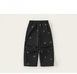 Détail du pantalon noir pour filles avec broderies de nœuds roses et jambes plissées