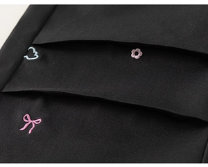 Détail du pantalon cargo enfant avec broderies de nœuds et de fleurs sur tissu noir soigné