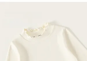 Close-up of the elegant ruffle edge neckline on a soft beige long-sleeve cotton undershirt