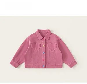 Détail d'une veste en jean rose avec poches en forme de cœur et boutons colorés pour fille
