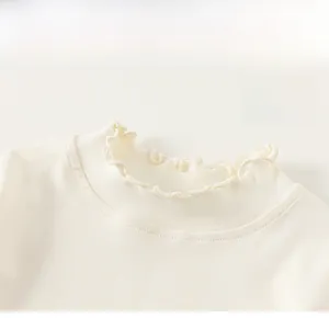 Detail of ruffled round collar and soft knit texture on cream long sleeve girls top