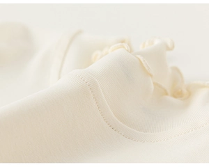 Detailed close-up of the ruffled collar on a cream ribbed knit cotton girl's undershirt