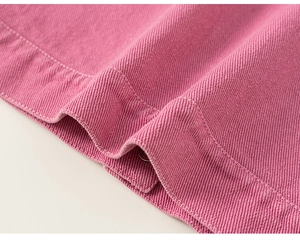 Gros plan de l'ourlet en denim rose avec coutures régulières et un bouton en métal argenté