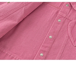 Détail de la texture en denim rose avec boutons argentés et coutures doubles soignées
