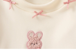 Detail van een crème shirt met lange mouwen, roze strikjes en borduursel van een pluche konijn